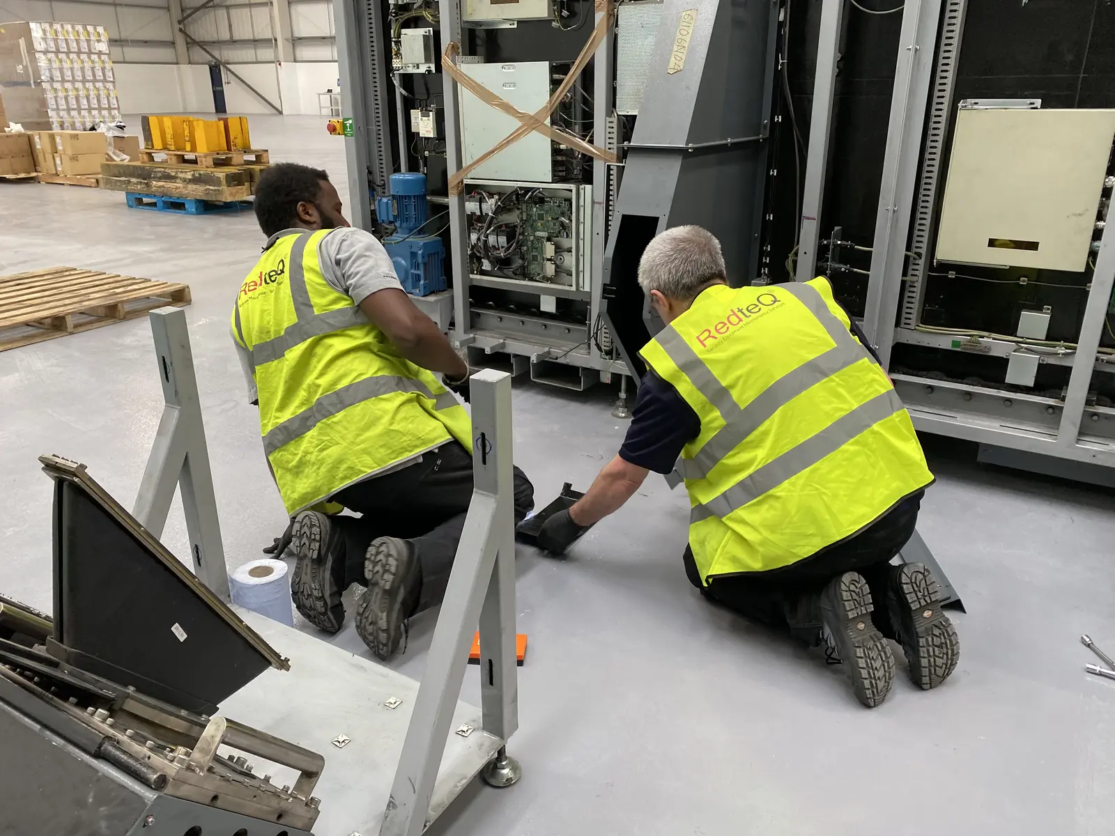 Two RedteQ engineers in hi-vis installing a security X-ray machine